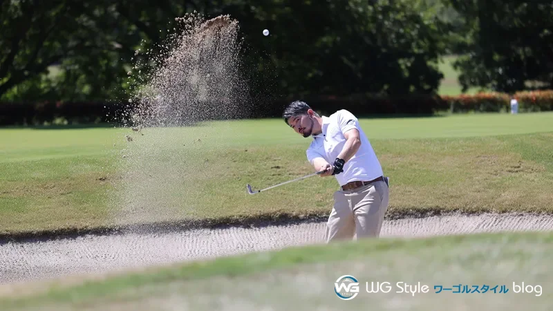 バンカーでサンドウェッジのショット直後、砂が舞い上がりボールが高い弾道で飛んでいる30代男性