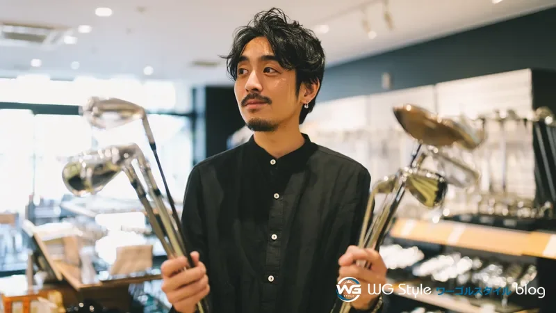 ゴルフショップで大量のクラブを抱えて迷っている初心者男性（クラブ選びの失敗イメージ）