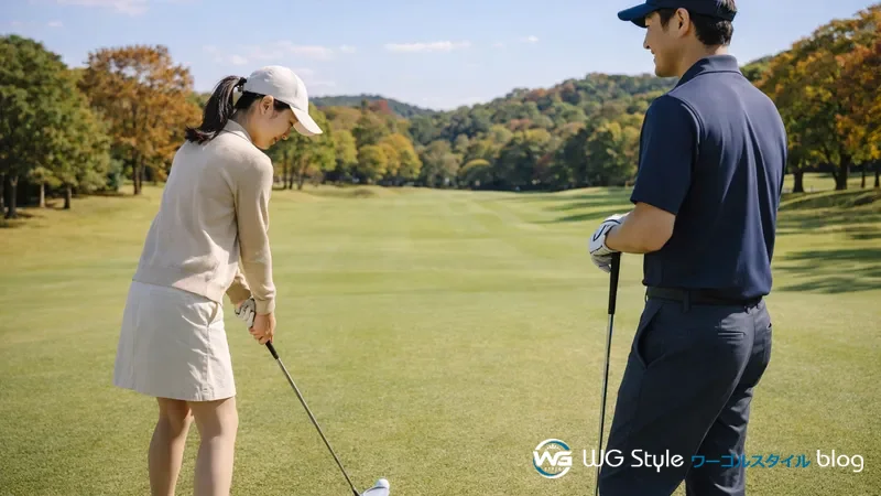 秋のゴルフコースで女性がアドレスし男性が隣で見守る季節に合ったゴルフコーデの場面