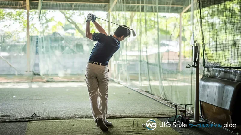 30代日本人男性がゴルフ練習場の打席で7番アイアンのハーフスイングを行っている