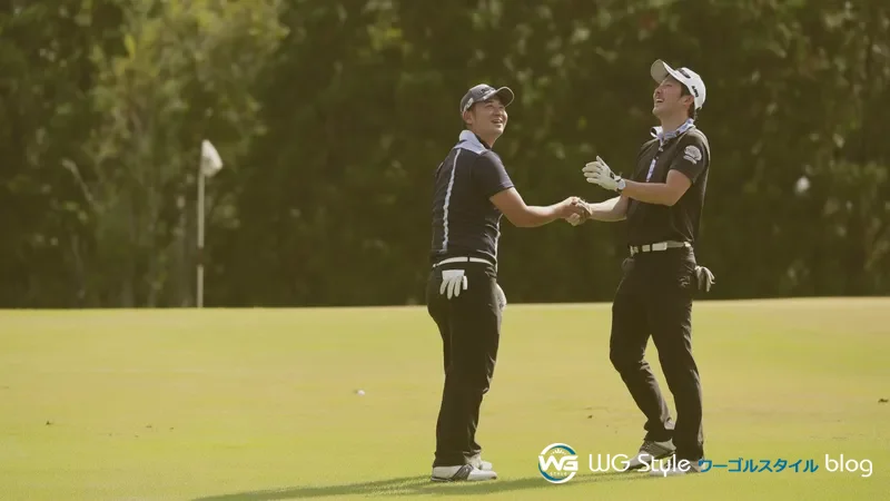 2人の30代日本人男性がゴルフコースでナイスショット直後に笑顔で称え合っている