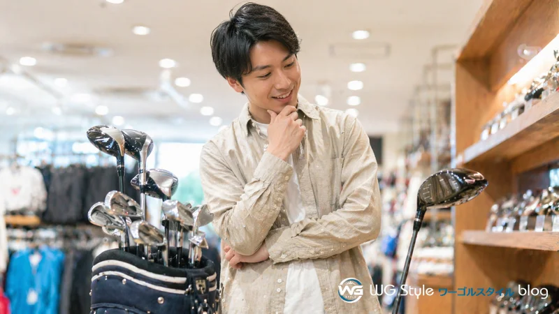 ゴルフショップで単品ドライバーと初心者クラブセットを見比べて選んでいる男性