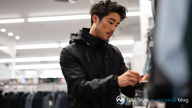 ゴルフ用品店でレインジャケットを試着しストレッチ性を確認しながら商品タグをチェックしている30代男性