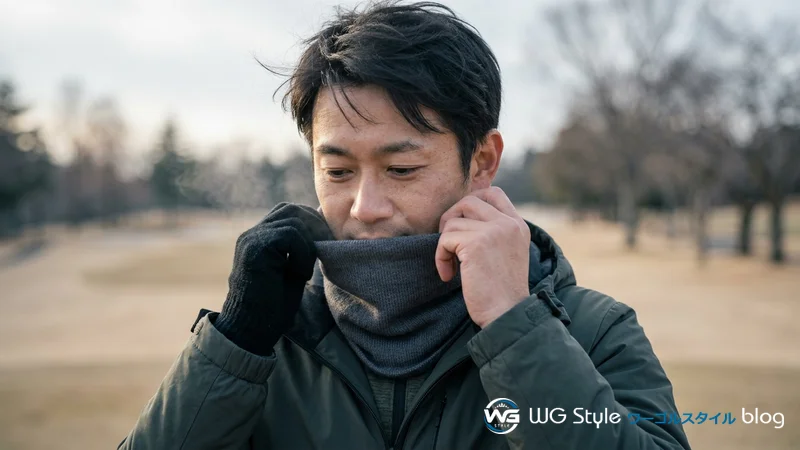 ネックウォーマーをあごの下まで引き上げて風を防ぐ日本人ゴルファーの首元のクローズアップ